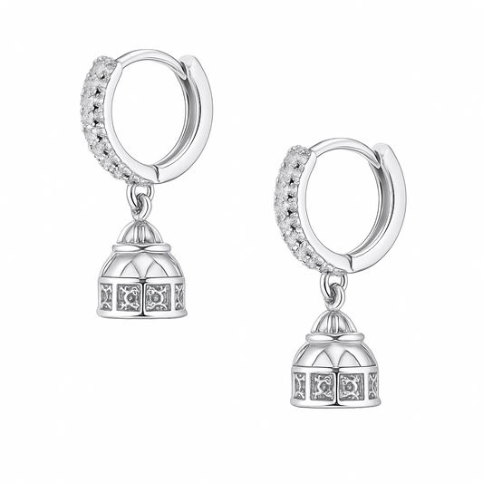 Silver hoop earrings with architectural design charms on a white surface with a flower in the background